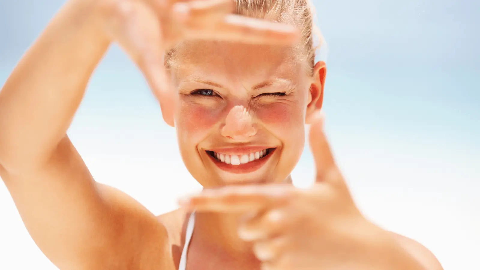 Woman with sun-flushed, dewy skin framing her face with her hands outdoors in humid weather